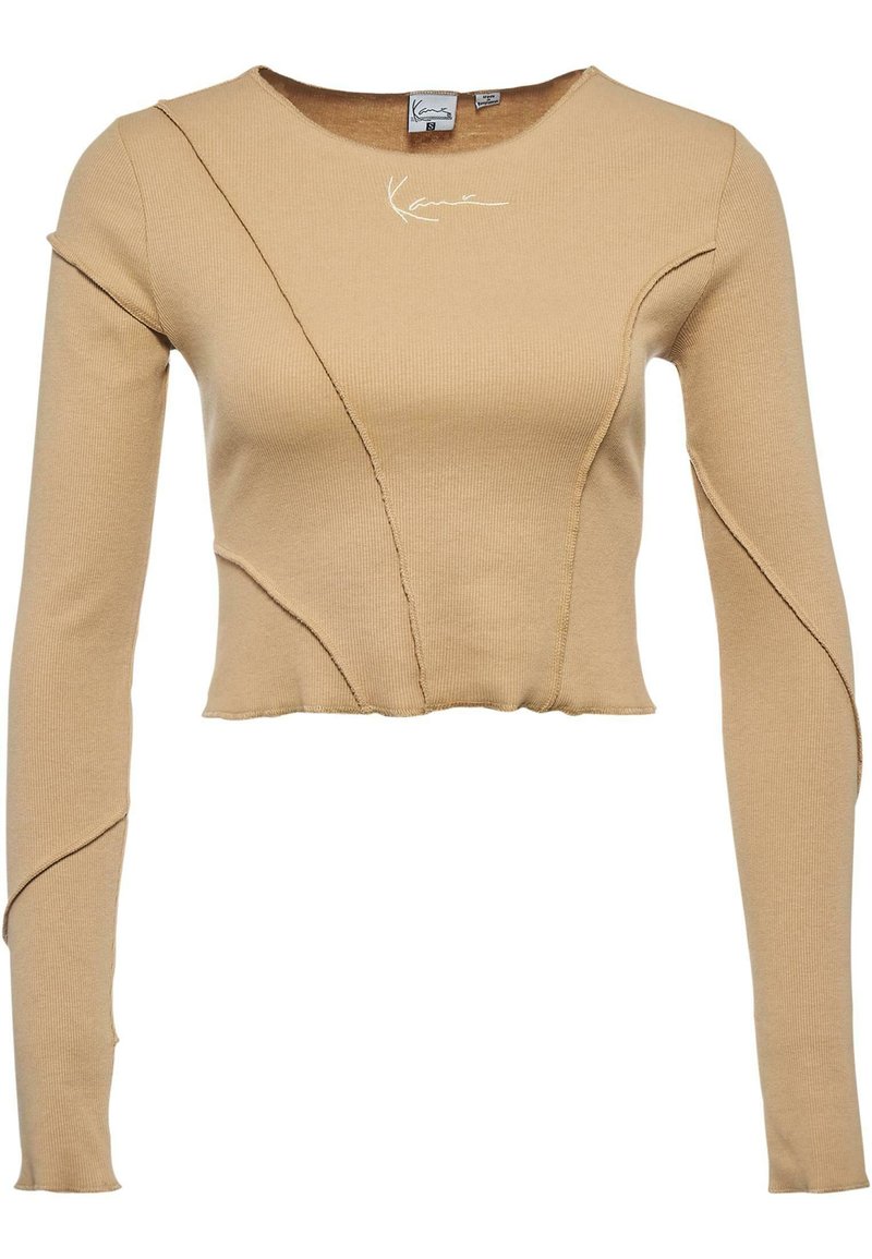 Beige ribbad pitkähihaine paita, jossa on ainutlaatuiset saumat, lyhyempi malli ja huomaamaton logotaito kaulan lähellä. Pehmeä koostumus ja istuva siluetti.