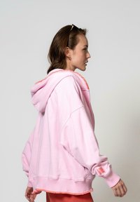Hoodie oversize rosa con una finitura testurizzata corallo sul cappuccio e sull'orlo. Presenta dettagli sui polsi e una vestibilità rilassata, realizzato in tessuto morbido.