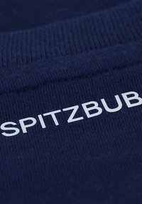Marineblauwe stof met een ribbelstructuur, met het woord "SPITZBUB" in vetgedrukte witte letters. Het ontwerp is eenvoudig en rechttoe rechtaan.