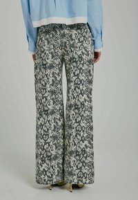 Pantaloni cu picioare late, cu un design în imprimeu de șarpe alb și negru, realizați dintr-un material texturat, având talie înaltă și o siluetă fluidă.