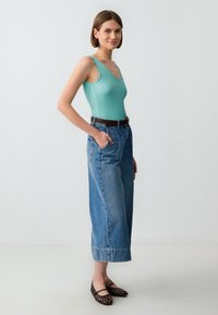 Body en maille bleu clair, pantalons large en jean bleu taille haute, ceinture marron et ballerines en raphia noires. Design simple et décontracté.