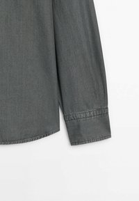 Manche longue d'une chemise unie gris foncé avec un poignet simple, présentée sur fond blanc. Aucun bouton ni motif visible.