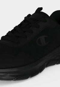 Baskets de sport noires avec dessus en mesh et synthétique, fermeture à lacets et logo sur le côté au-dessus d'une semelle épaisse en caoutchouc.