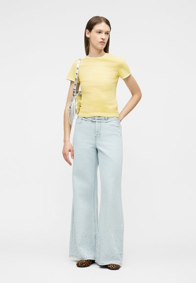 Γυναίκα με κίτρινο κοντομάνικο πουκάμισο, ανοιχτό γαλάζιο τζιν φαρδιάς γραμμής με λουλουδάτα σχέδια, παπούτσια με λεοπάρ σχέδιο και ασημί τσάντα ώμου.