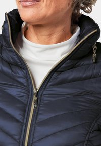Doudoune marine à col haut, avec un matelassage en chevrons horizontal, des zips dorés et une couche intérieure blanche. Texture douce et lisse.
