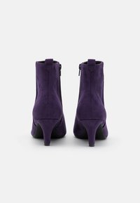 Botines de ante púrpura con puntera ligeramente puntiaguda, cremalleras laterales y un tacón bajo y afilado. Textura suave con acentos mínimos.