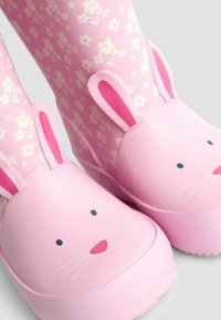 Różowe kalosze dla dzieci z białymi wzorami kwiatowymi oraz twarzami króliczków, z uszami z przodu i czarnymi oczami oraz wąsami.