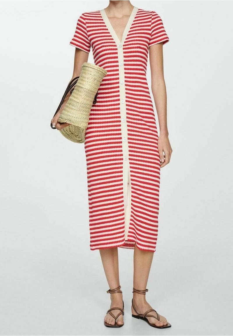 Femme portant une robe midi à boutons rayée rouge et blanche, tenant un sac en paille tressée et portant des sandales plates marron à lanières.