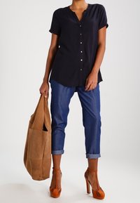 Marineblå kortærmet bluse med knapper foran, lyseblå opsmøgede jeans, brun ruskinds taske og orange højhælede sko.