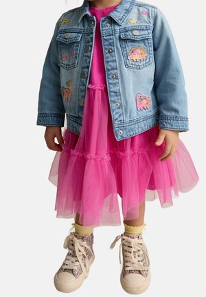 Enfant portant une veste en denim bleue avec des patchs animaux, une robe en tulle rose, des chaussettes jaunes et des baskets hautes pailletées.
