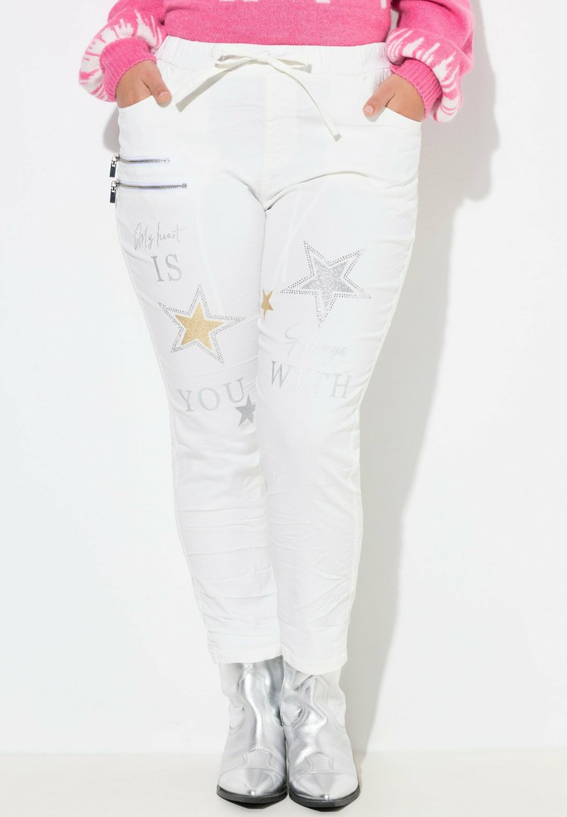 Witte joggingsbroek met metalen zilveren en gouden sterpatronen, voorzakken met rits en een tailleband met trekkoord. De textuur lijkt glad.