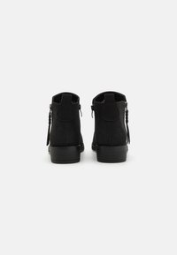 Botines negros con acabado de cuero suave, tacón bajo apilado, cremalleras laterales y detalle de lengüeta en la parte trasera. Diseño clásico y estructurado.