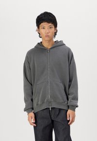 Grå zip-up hoodie med avslappnad passform, dragsko vid huvan, fickor fram och ribbade ärmmuddar. Tillverkad av mjukt bomullsblandat tyg.