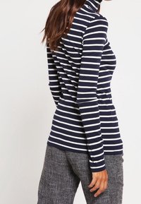 Maglione a collo alto a righe navy e bianche con maniche lunghe, tessuto morbido, design aderente e colletto a coste, abbinato a pantaloni grigi con texture.