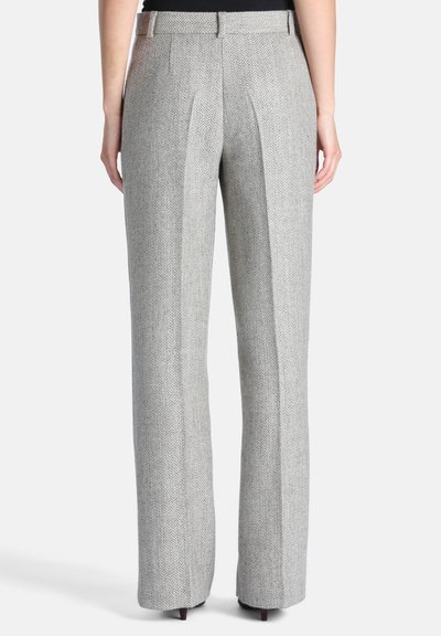 Personne porte un pantalon gris à motif chevrons, sur mesure, avec des jambes droites et des poches arrière, debout devant un fond clair.
