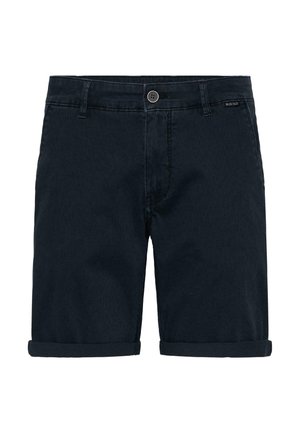 Tumesinised teksapüksid, millel on üles keeratud ääred, nupuga kinnis, vööaugud ja esised taskud, laotatud valgele taustale.