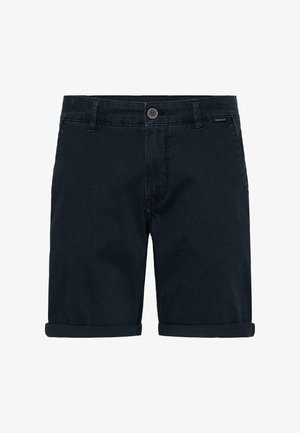 Tumesinised teksapüksid, millel on üles keeratud ääred, nupuga kinnis, vööaugud ja esised taskud, laotatud valgele taustale.