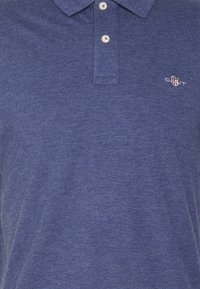 Blaues Poloshirt mit zwei weißen Knöpfen und einem kleinen, auf der linken Brust gestickten GANT-Logo.