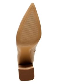 Zapato de tacón alto color beige claro con punta puntiaguda. Parte superior de cuero suave y suela exterior texturizada con ranuras para mayor agarre. Diseño de tacón ancho.