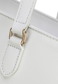 Sac à main blanc texturé avec un léger motif grainé, présentant un fermoir en métal doré et des détails de couture sur la poignée.