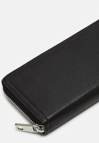 Czarny skórzany portfel o teksturowanym wykończeniu, z srebrnym zamkiem błyskawicznym i minimalnym logo na powierzchni. Kompaktowy prostokątny kształt.