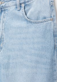 Gros plan sur un tissu en jean bleu clair montrant la partie supérieure d'un jean avec une poche avant, une boucle de ceinture et des rivets en métal.