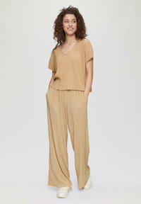 Beige geplooide top en wijde broek set, met een v-hals en korte mouwen, met een gestructureerde afwerking. Gemaakt met witte sneakers.