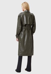 Trench coat in pelle verde oliva con cintura, spalline e lunghezza fino al polpaccio. Texture liscia e design strutturato.
