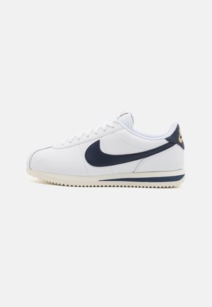 Zapatillas Nike con parte superior de cuero blanco, acentos en color marino, suela de goma texturizada y detalles de costura clásicos.