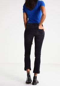 Jeans in denim nero dal design aderente e lunghezza cropped, abbinati a una camicia blu a maniche corte e stivali neri alla caviglia.
