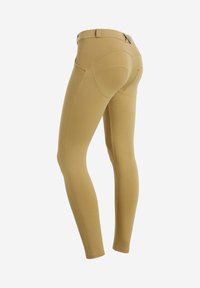 Leggings aderenti color beige con cuciture curve sul retro, una vita e dettagli di cucitura sottili. Realizzati in tessuto elastico e liscio.