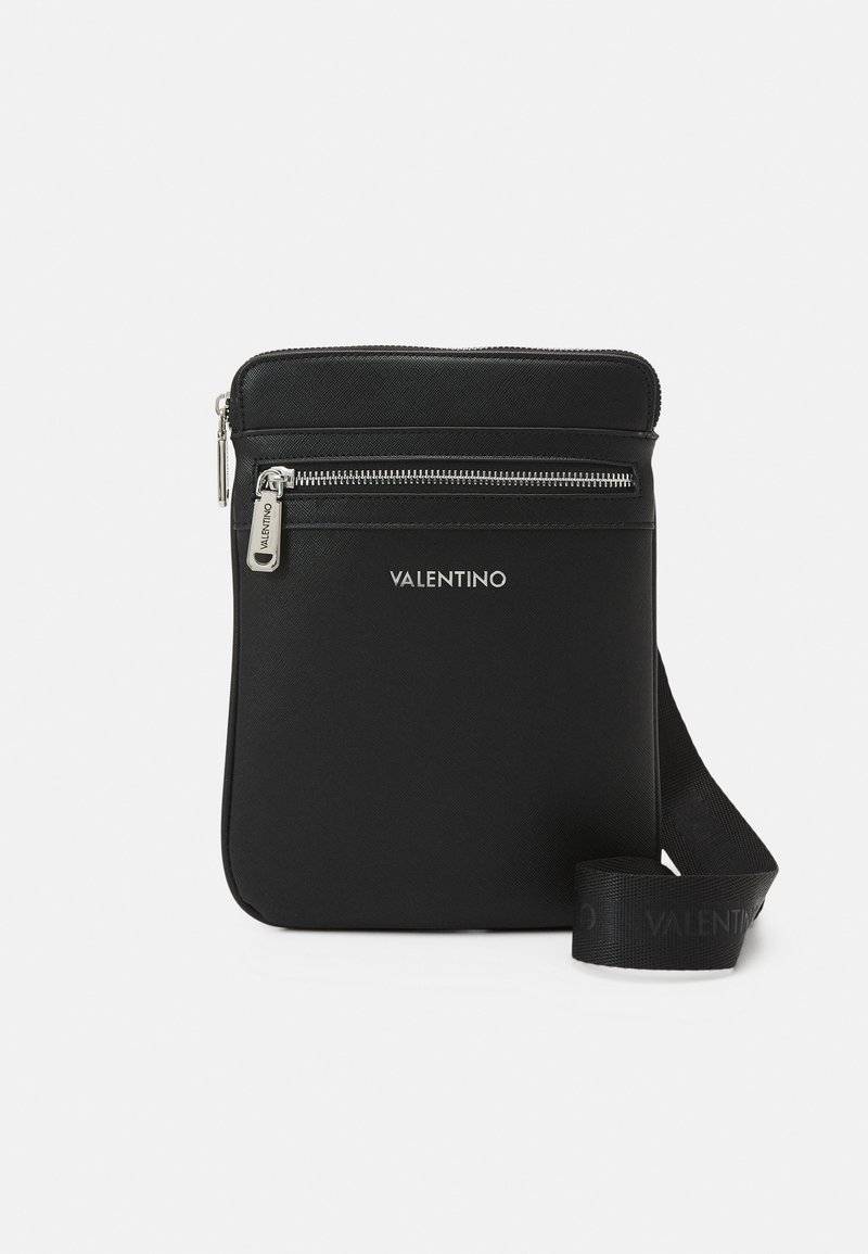 Černá nylonová taška přes tělo s zipovým uzávěrem a stříbrným kováním. Obsahuje potištěné logo a plochý nastavitelný popruh.