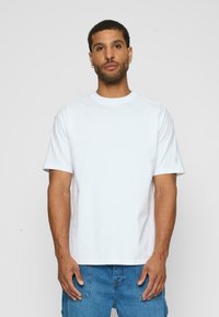 Hvid bomulds t-shirt med korte ærmer og rund halsudskæring. Har et diskret logo på venstre ærme. Klassisk pasform med en glat tekstur.