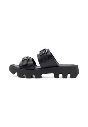 Black leather sandals with two adjustable buckles, a flat heel, and a chunky tread outsole featuring large, angled cutouts.
