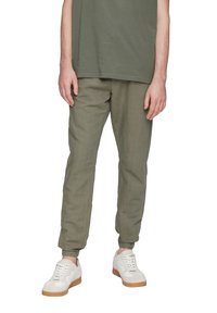 Zielone lniane spodnie dresowe z elastycznymi mankietami, bocznymi szwami i luźnym krojem, w połączeniu z białymi trampkami z gumową podeszwą.