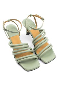 Sandali con tacco in pelle verde con ampie fasce, design con punta quadrata e soletta beige, dotati di un piccolo tacco a blocco.