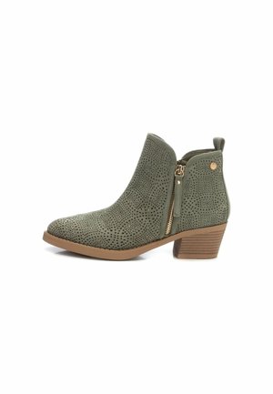 Botín verde de tobillo fabricado en material perforado, con una cremallera lateral, herrajes decorativos y un tacón apilado con una base texturizada.