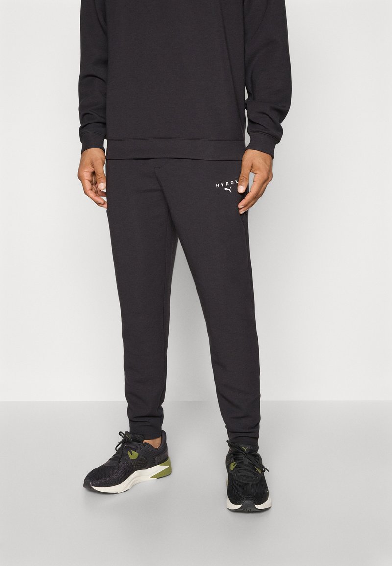Schwarzer Baumwoll-Sweatshirt und passende Jogginghosen mit dezentem Logodruck, gerippten Bündchen und schmal zulaufendem Bein, kombiniert mit schwarzen Sportschuhen.