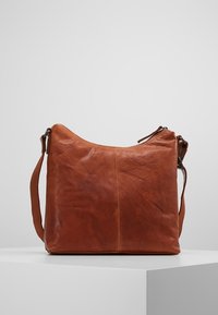 Leren tas in bruin met een zachte textuur, een slungelige vorm en een enkele verstelbare schouderband. Heeft minimale stiksels en een eenvoudig ontwerp.
