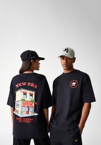 Black t-shirts with graphic designs: one features a café scene, the other has a logo. Caps are black and light grey with embroidered details.