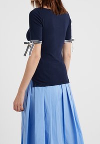 Navy short-sleeve top with striped ribbon accents on cuffs, fitted design, and soft fabric. Paired with a pleated blue skirt.