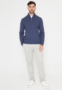 Marineblauer Zip-Kragen-Pullover aus weichem Material, kombiniert mit hellgrauen Hosen und weißen Sneakers. Schlichtes Design mit gerippten Bündchen und Saum.