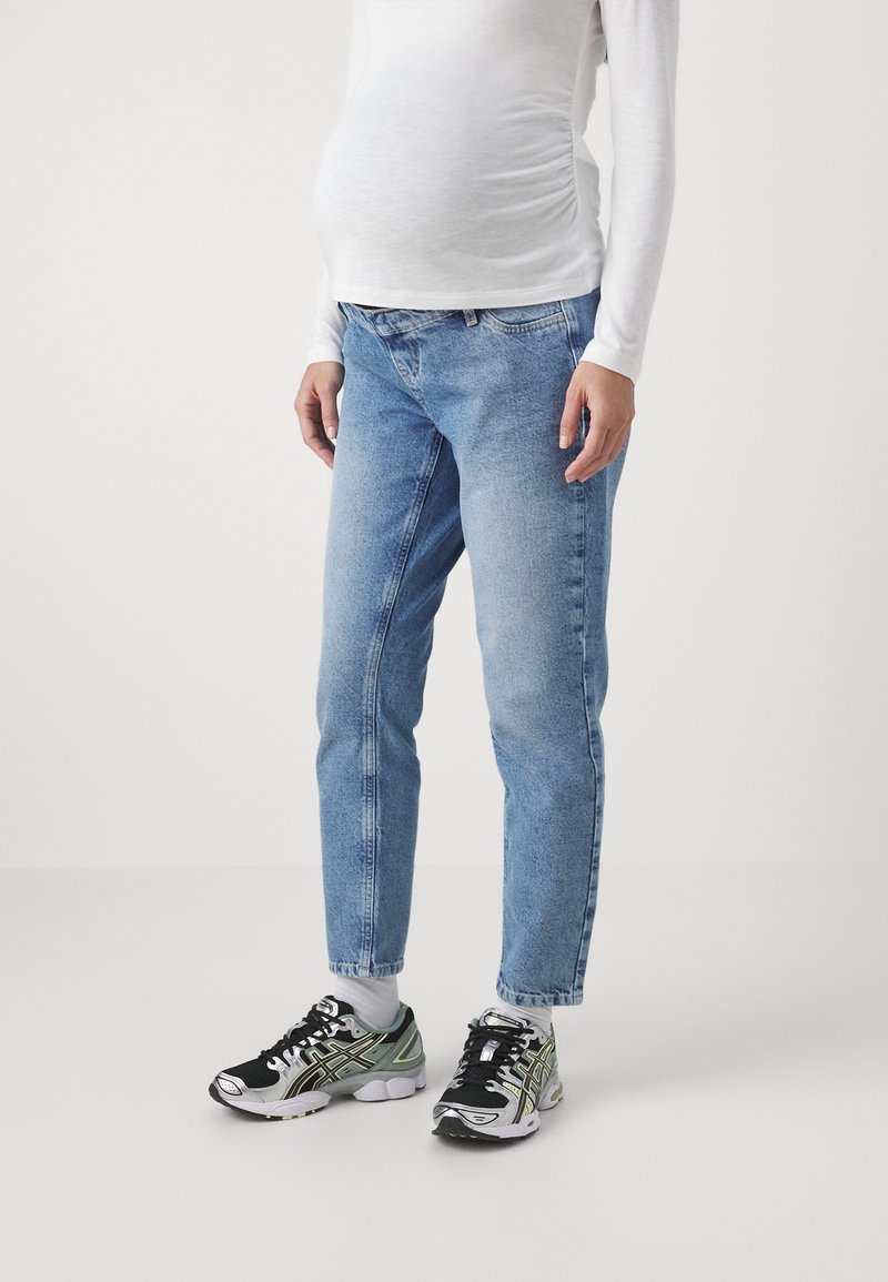 Ljusblå denimjeans med rak passform, bärs med svarta och grå träningsskor. Överdelen är en vit långärmad skjorta.