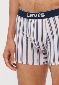 Levi's férfi boxeralsó, sötétkék elasztikus derékkal, amelyen kék és fehér függőleges csíkok láthatók egy világos rózsaszín háttéren.