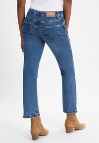 Vaqueros de mezclilla azul con un corte recto, que cuentan con bolsillos traseros, una etiqueta de cuero con marca en la cintura y detalles de costura sutiles.