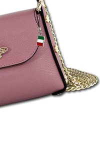 Sac en cuir rose avec une bandoulière en chaîne dorée, ornée d'un emblème de papillon et d'un charm en forme de drapeau italien attaché à la fermeture éclair.