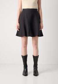 Jupe noire évasée en tissu léger, avec une surface texturée et une taille mi-haute, associée à des bottes de cowboy noires à motifs.