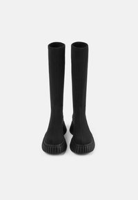 Botas negras hasta la rodilla con un upper de tela suave y una suela de goma texturizada con un diseño estriado, que proporciona una forma moderna y estilizada.