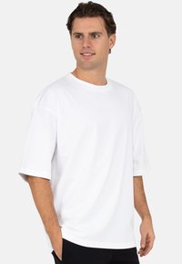 Witte oversized T-shirt met korte mouwen, ronde hals en zijslitsen. Gemaakt van gladde stof met een eenvoudig, strak ontwerp.