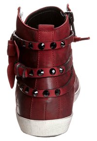 Rode leren enkelboot met zwarte studsriemen, ritsluiting en een witte rubberen zool. Subtle textuur en een afgeronde neusdesign.